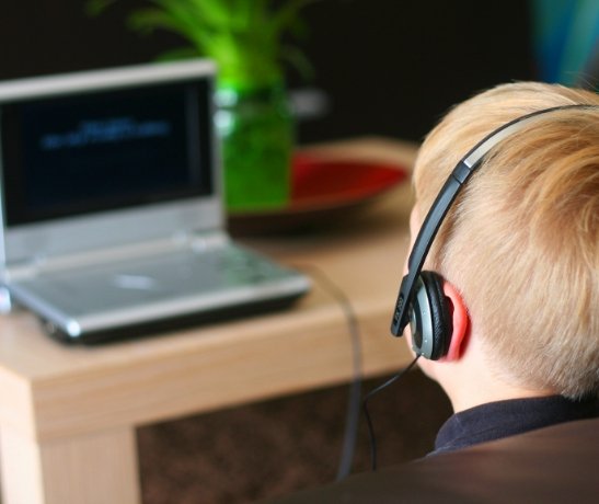 zeigt einen Jungen mit Kopfhörer vor einem Laptop